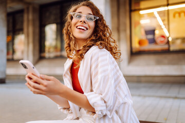 Attractive woman smiling as she uses her phone walking down the street in the city. Technology,...