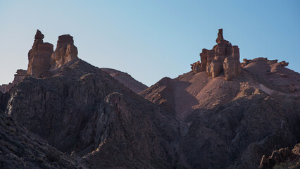 The rugged beauty of a desert landscape is captured as the sun casts its glow on sandstone spires, which stand proudly against a clear, pale sky.