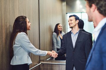 Handshake, greeting and business people in elevator at office for formal introduction with meeting. Happy, welcome and finance advisor shaking hands with client in lift for contract deal or agreement