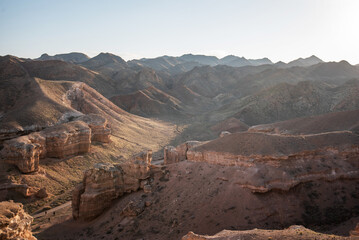 Golden sunlight bathes the rugged landscape of a vast canyon, where towering red rock formations...