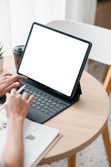 Fototapeta premium Hands typing on a tablet with a blank screen in a bright workspace, featuring coffee and documents on a wooden table.