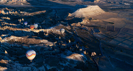 At dawn, hot air balloons float over a sprawling valley shadowed by undulating mountains, their...