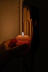 Burning candle in hand near intercom in darkness. Power outage due to war in Ukraine