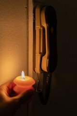 Burning candle in hand near intercom in darkness. Power outage due to war in Ukraine