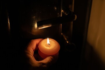 Burning candle in hand near door lock in darkness. Power outage due to war in Ukraine