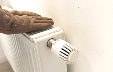 Girl in glove adjusting heating radiator thermostat near white wall, closeup