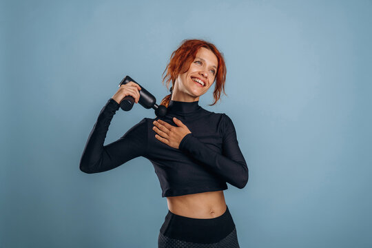 Fototapeta Black electric massager, in fitness clothes. Woman is in the studio against background