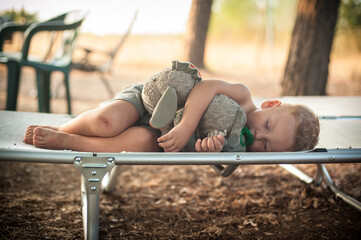 A young child peacefully sleeping on a cot cuddling a stuffed animal in a serene outdoor setting...