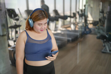 Obese asian woman Enjoy listening to music. Fat Female with headphones smart phone after workout at Gym