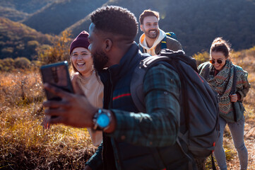 Smiling group of friends having fun while hiking together on hill at sunset and making video blog with smart phone.