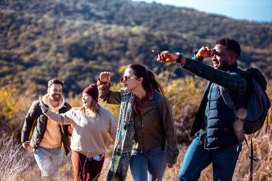 Smiling group of friends having fun while hiking together on hill at sunset.