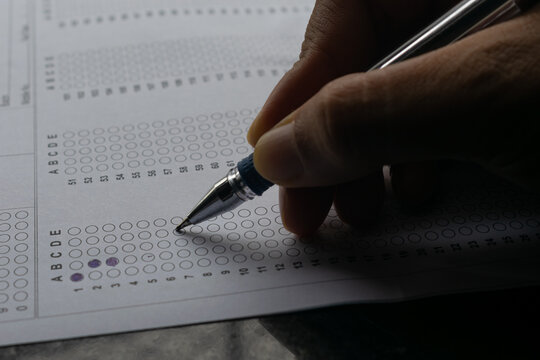 Hand of a person marking answers in OMR sheet. NEET, JEE exam centre hall student teacher time leak paper question marks tick scam cheating copy AIR rank coaching court case result KnowledggeForAll