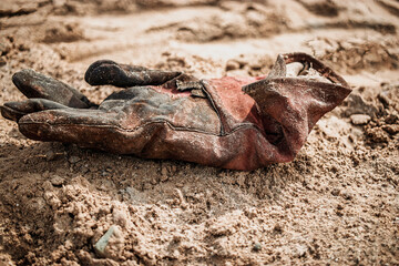An old, weathered work glove rests in the sun-baked soil, telling the story of hard labor and...