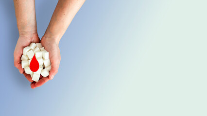 Sugar cubes and blood drop in women's hands symbolizing high blood sugar and diabetes. World...
