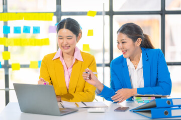 Two Asian businesswomen are deeply engaged in a discussion about data analysis work on a computer...