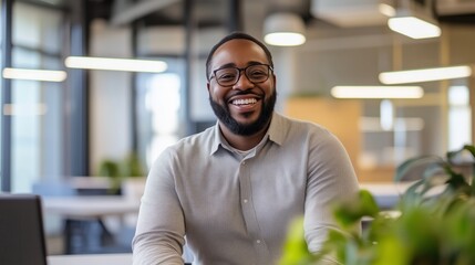 A man with glasses is smiling and sitting in front of a plant