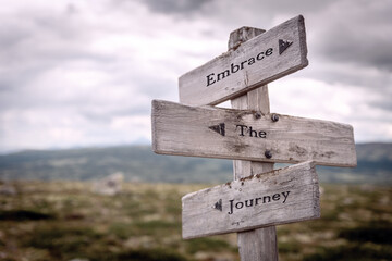 embrace the journey text quote written on wooden signpost at the crossroads outdoors in nature.