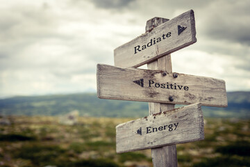 radiate positive energy text quote written on wooden signpost at the crossroads outdoors in nature.