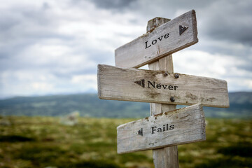 love never fails text quote written on wooden signpost at the crossroads outdoors in nature.