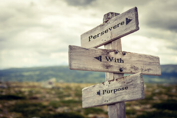 persevere with purpose text quote written on wooden signpost at the crossroads outdoors in nature.