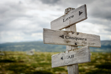 love conquers all text quote written on wooden signpost at the crossroads outdoors in nature.