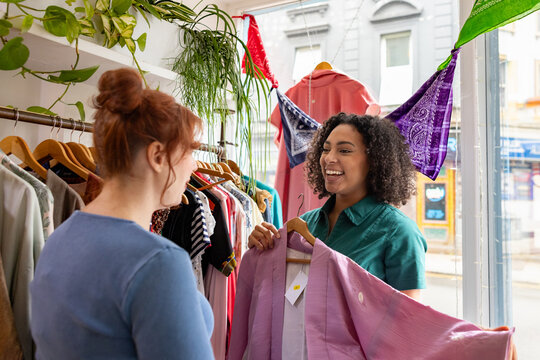 Female friends shopping in a thrift store having fun trying on clothes