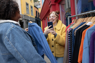 Young female taking photo of friend trying on clothes at a street market