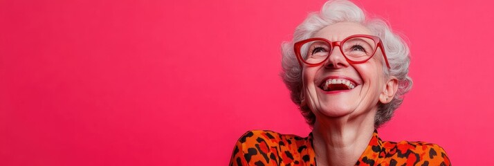 Cheerful elderly woman with white hair in vibrant outfit against a pink background.