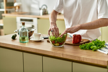 A youthful man mixes a vibrant salad, embracing healthy cooking in a stylish kitchen.