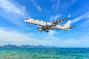 Obraz premium Plane fly ready for landing approaching over ocean bay cirrus clouds and on horizon hills landscape and buildings of the city.