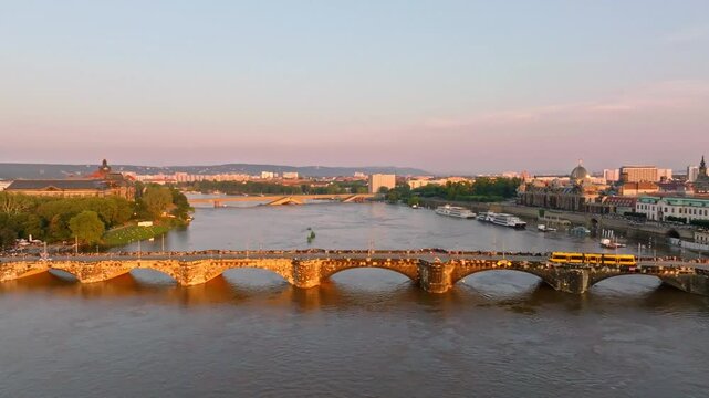 Drone video of Dresden during a flood with warm light illuminating the scene. A tram crosses a bridge, while the damaged Carola Bridge is visible in the background.
