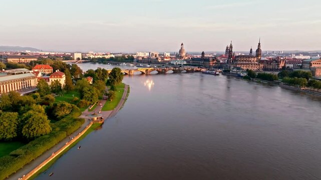 Drone video of Dresden during a flood with warm light illuminating the scene. Two tram crosses a bridge, while the damaged Carola Bridge is visible in the background.  Drone move forward.