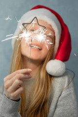 Sparkler in shape of star in hand beautiful girl with long red hair in Santa hat on grey background