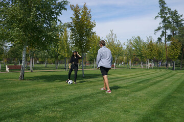 A couple plays soccer together on a lush, green field. They kick the ball back and forth, laughing...
