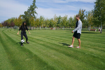 A couple plays soccer together on a lush, green field. They kick the ball back and forth, laughing...