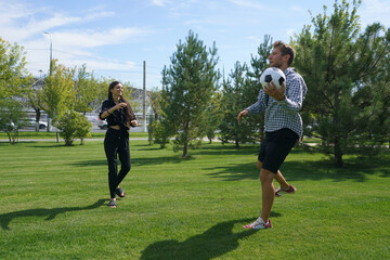 Fototapeta premium A man and woman engage in a lively game of soccer on a warm summer day, laughing and having fun as they play in a lush green park surrounded by trees