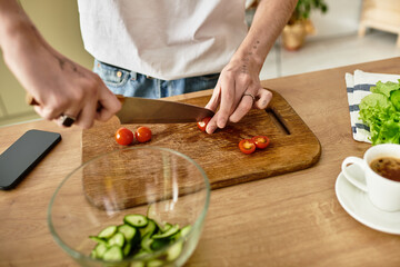 A handsome young man skillfully chops tomatoes while creating a vibrant salad in a stylish kitchen setting.