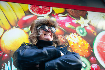 Confident woman in aviator hat and sunglasses posing against vibrant fruit mural © Ktn