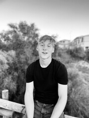 Portrait of a teenage handsome blond guy looking with smile to camera, monochrome photography outdoors 