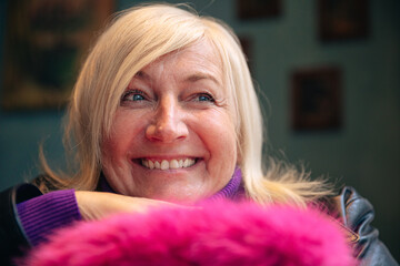 Joyful senior woman smiling in cozy indoor setting with pink accents