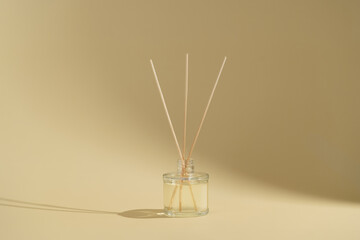 Transparent glass bottle of aroma reed diffuser or home fragrance with rattan sticks on beige isolated background with shadow. Decoration and aromatherapy concept. Eco-friendly luxury aroma scent.