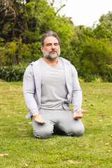 Mature man meditating outdoors on grass, finding peace and relaxation