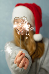 Heart shaped bengal fire in hand beautiful girl with long red hair New Year hat on grey background 