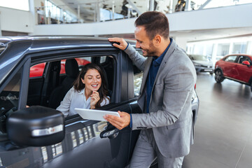Smiling Woman in Car Discussing Deal with Salesman at Showroom