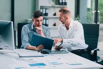 Fototapeta premium Two businessmen working together Analyze financial reports with charts and graphs while using the calculator to calculate budget, income, taxes, business growth. Startup business idea.