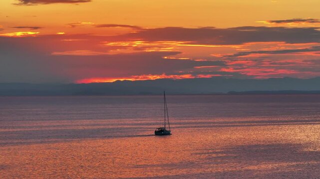 lonely sailboat on the Ionian sea at sunrise with beaming orange and yellow sunny hues in Zakynthos greece AERIAL STATIC