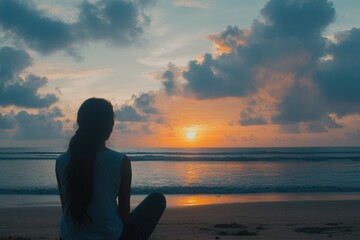 Fototapeta premium A woman sits on the beach, gazing at the sunset