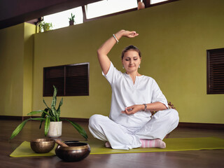 A woman practices meditation in Kundalini yoga, sits in a comfortable lotus position on a mat in a...