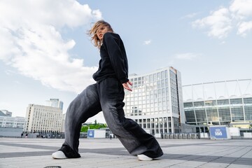 Young woman dancing on city plaza with modern architecture backdrop
