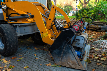 A yellow loader with a black bucket is parked on a brick driveway. The bucket is raised, revealing...